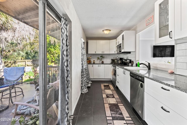 kitchen with a textured ceiling, dark stone countertops, appliances with stainless steel finishes, decorative backsplash, and white cabinets