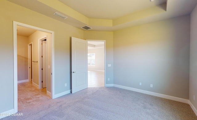 unfurnished bedroom featuring a tray ceiling and light colored carpet