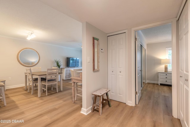 hallway featuring light wood finished floors, baseboards, and ornamental molding