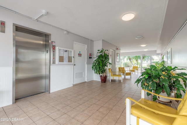 hallway with visible vents, elevator, a textured ceiling, and wainscoting