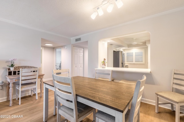 dining room featuring light wood finished floors, a textured ceiling, and ornamental molding