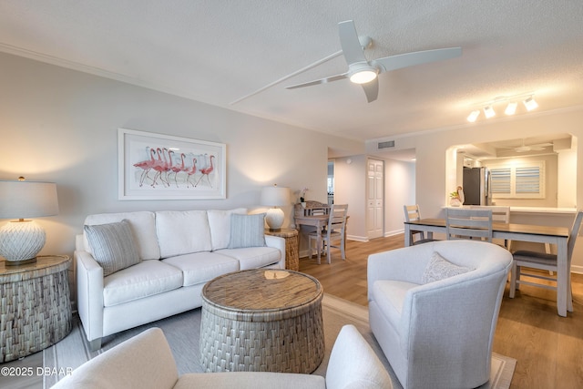 living room with ornamental molding, a textured ceiling, a ceiling fan, and wood finished floors