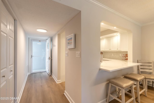 corridor featuring light wood-style flooring, a textured ceiling, baseboards, and ornamental molding