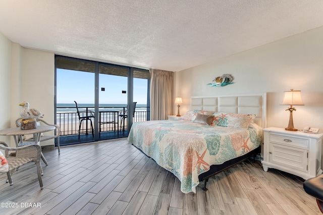 bedroom with a textured ceiling, access to outside, floor to ceiling windows, and a water view