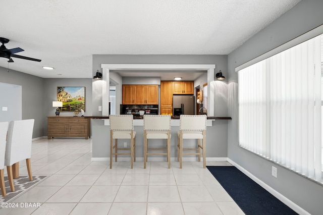 kitchen featuring light tile patterned flooring, kitchen peninsula, a breakfast bar area, and stainless steel fridge