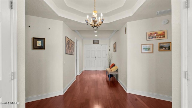 hallway featuring ornamental molding, dark hardwood / wood-style flooring, a tray ceiling, and an inviting chandelier