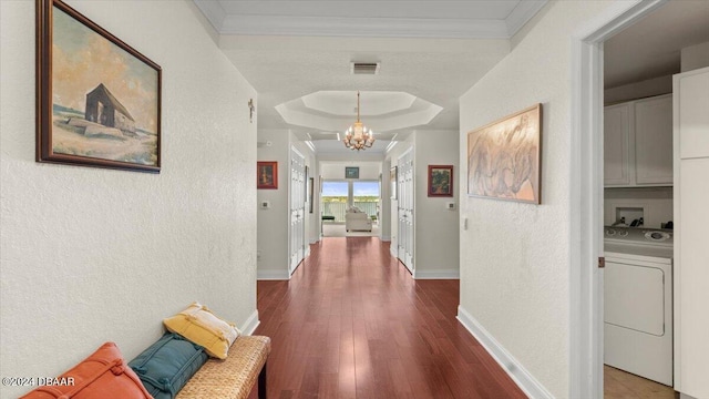 corridor with hardwood / wood-style flooring, ornamental molding, an inviting chandelier, washer / clothes dryer, and a tray ceiling