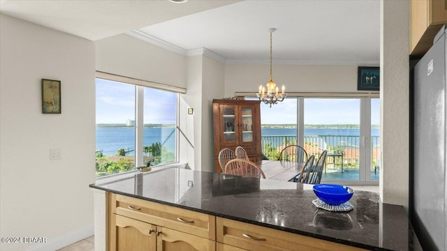 kitchen with hanging light fixtures, light brown cabinetry, an inviting chandelier, and a water view