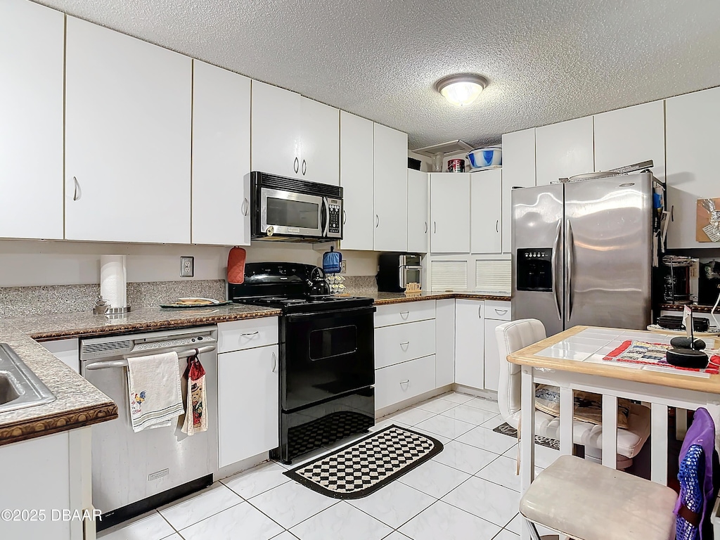 kitchen featuring stainless steel appliances, white cabinets, a textured ceiling, and light tile patterned floors