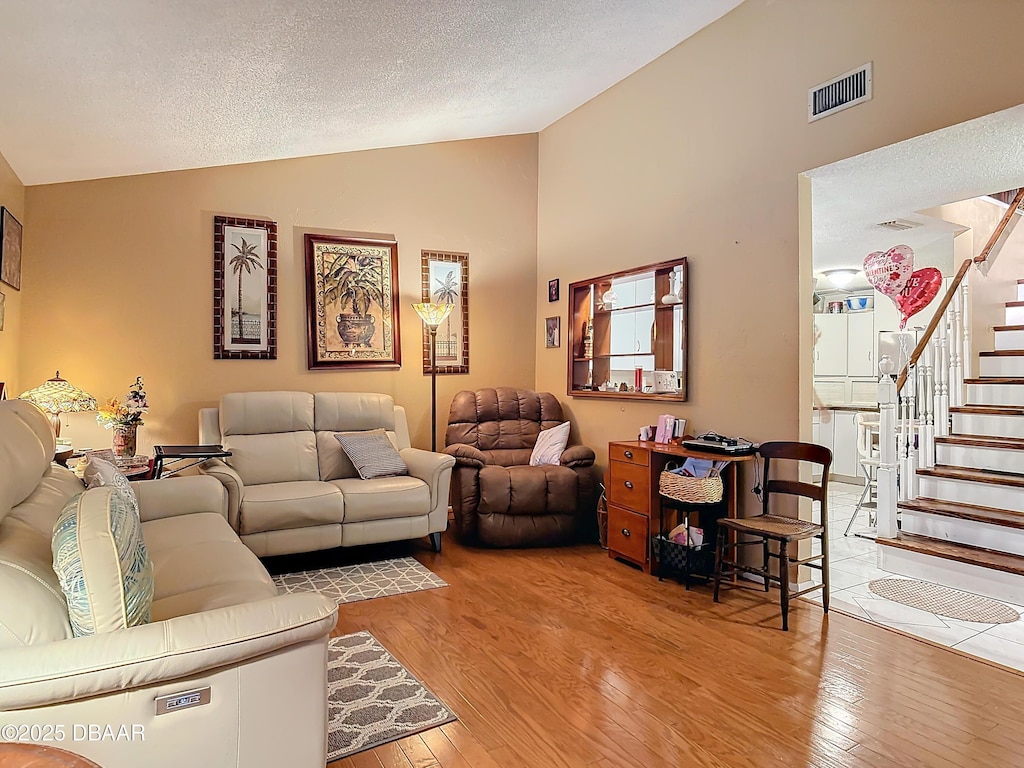 living area featuring vaulted ceiling, hardwood / wood-style floors, stairs, and visible vents