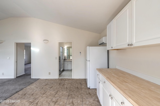 kitchen with baseboards, a wall unit AC, lofted ceiling, freestanding refrigerator, and white cabinetry