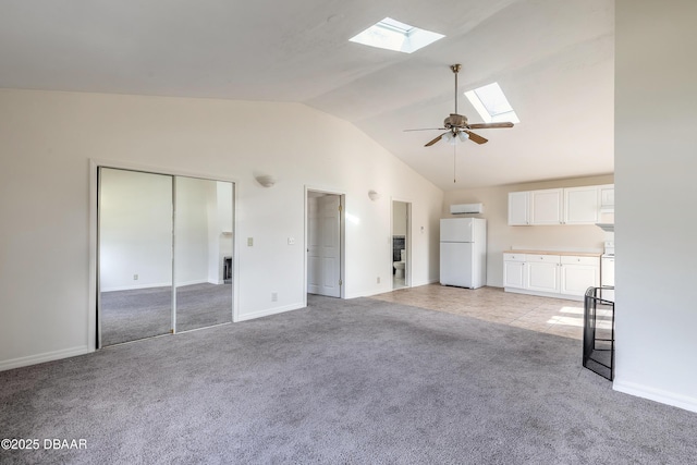 unfurnished living room featuring ceiling fan, high vaulted ceiling, light colored carpet, a skylight, and baseboards