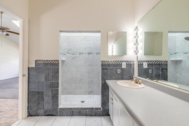 full bath featuring a wainscoted wall, ceiling fan, walk in shower, vanity, and tile walls