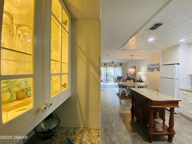 kitchen with light stone countertops, decorative light fixtures, hardwood / wood-style flooring, white fridge, and white cabinetry