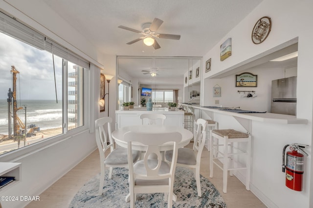 dining space with ceiling fan, light hardwood / wood-style floors, a textured ceiling, and a water view