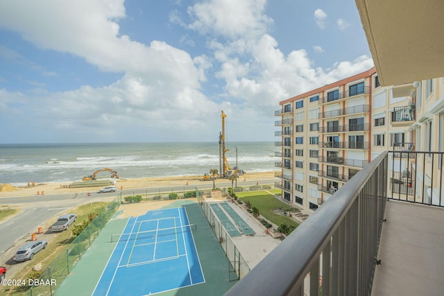 balcony featuring tennis court, a water view, and a beach view