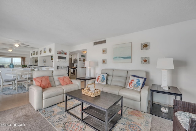 living room featuring ceiling fan, a textured ceiling, and light hardwood / wood-style floors