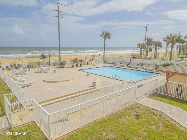 view of pool featuring a beach view, a water view, a lawn, and a patio area