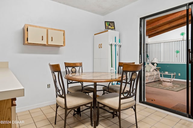 dining space featuring a textured ceiling, light tile patterned floors, and vaulted ceiling with beams