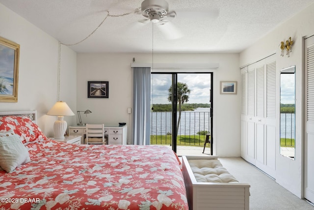 bedroom featuring a water view, access to outside, light carpet, and a textured ceiling