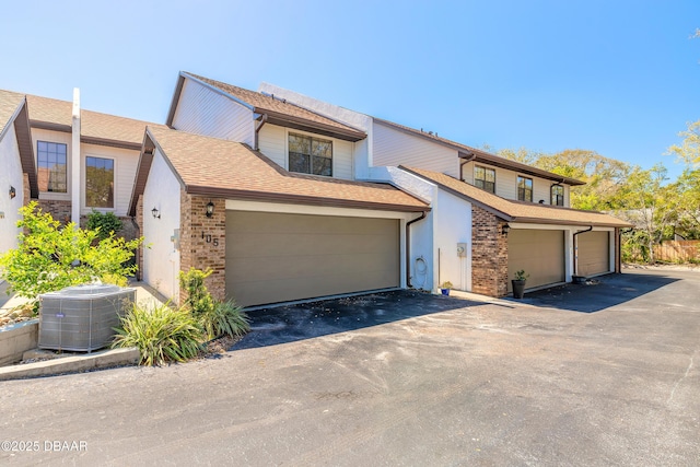 view of front of property with a garage, brick siding, central AC, and a shingled roof