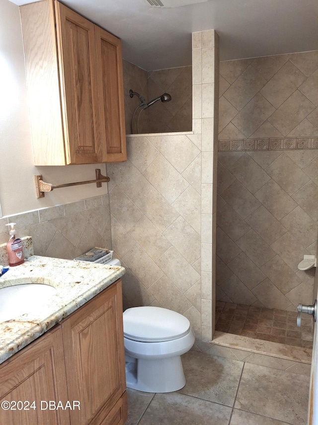 bathroom featuring tile patterned flooring, a tile shower, vanity, toilet, and tile walls