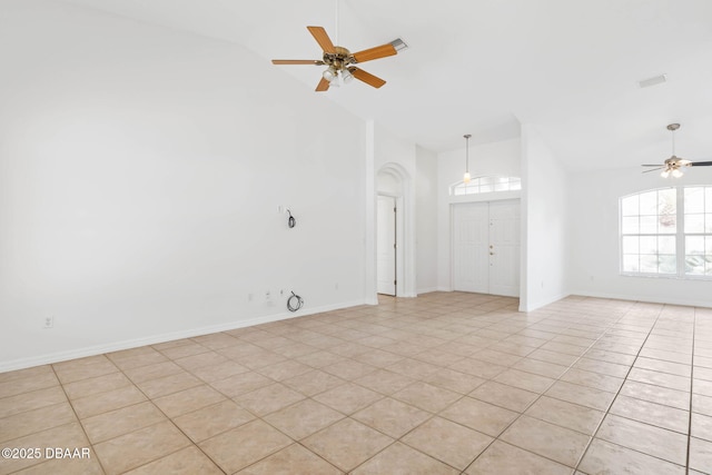 empty room with a ceiling fan, high vaulted ceiling, light tile patterned floors, arched walkways, and baseboards