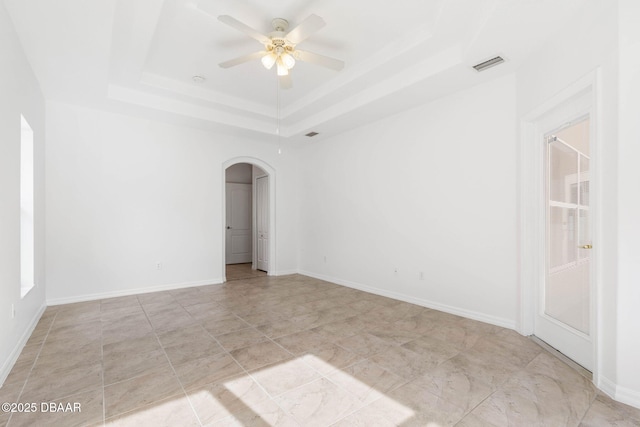 empty room with arched walkways, a tray ceiling, a ceiling fan, and baseboards