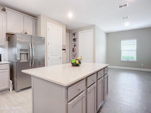 kitchen featuring light stone countertops, stainless steel fridge with ice dispenser, light wood-type flooring, and a kitchen island