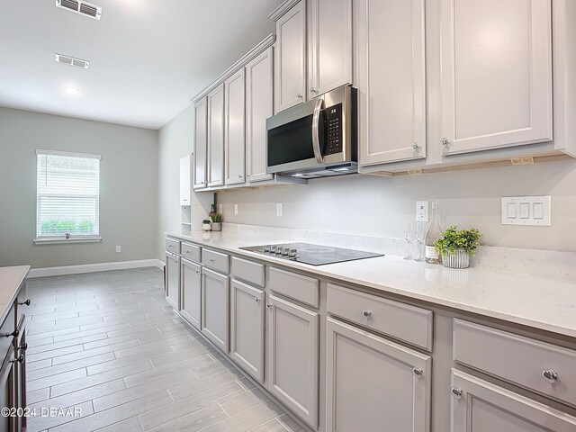4155 Clifden Dr, Ormond Beach, FL 32174 - kitchen with black electric cooktop, light hardwood / wood-style floors, gray cabinetry, and light stone counters