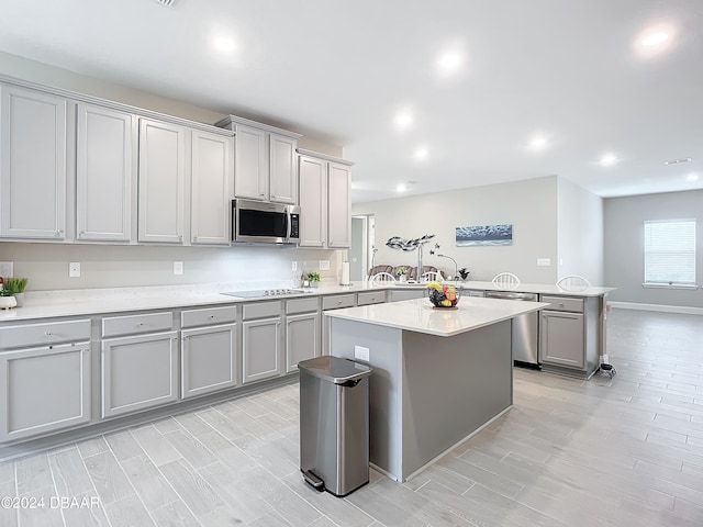 kitchen featuring light hardwood / wood-style floors, a center island, kitchen peninsula, gray cabinets, and appliances with stainless steel finishes