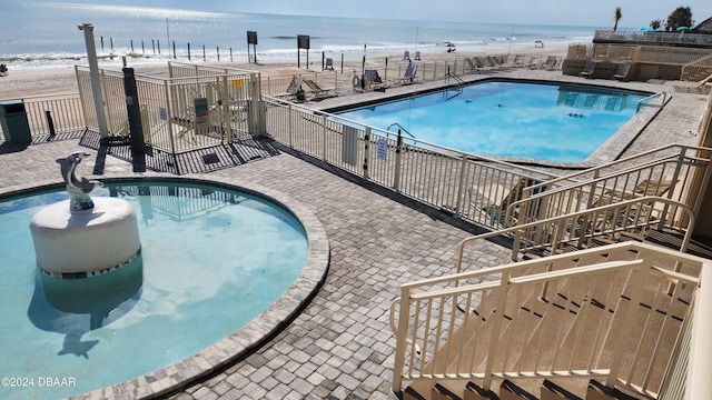 view of pool featuring a patio area, a view of the beach, and a water view