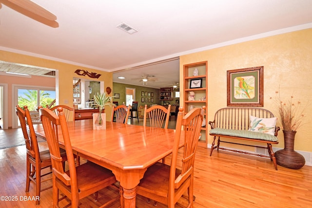 dining room featuring light wood-type flooring, built in features, ceiling fan, and crown molding