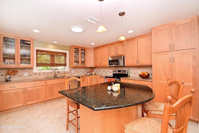 kitchen with sink, a center island, dark stone countertops, light brown cabinetry, and appliances with stainless steel finishes