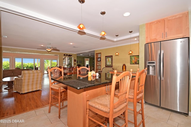 kitchen with hanging light fixtures, light tile patterned floors, ceiling fan, a kitchen bar, and stainless steel refrigerator with ice dispenser