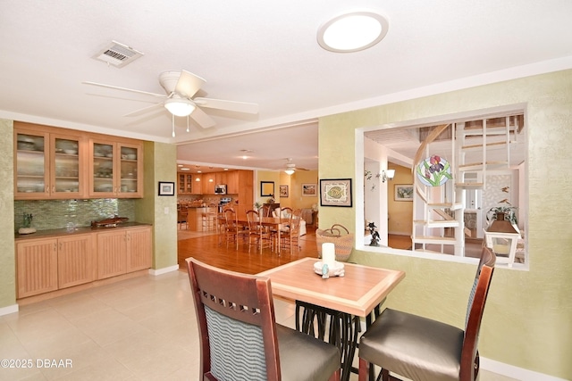 tiled dining space with ceiling fan and crown molding