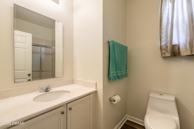 bathroom featuring baseboards, a shower with door, vanity, and toilet