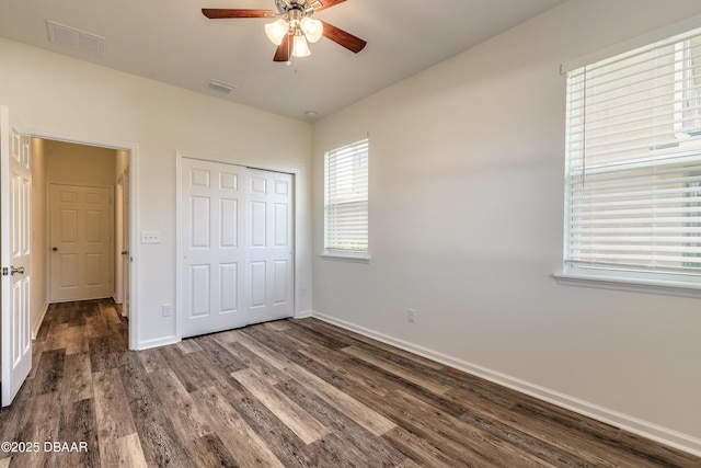 unfurnished bedroom featuring dark wood-style flooring, a ceiling fan, visible vents, baseboards, and a closet