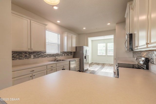 kitchen with stainless steel appliances, a sink, white cabinetry, light wood-type flooring, and tasteful backsplash