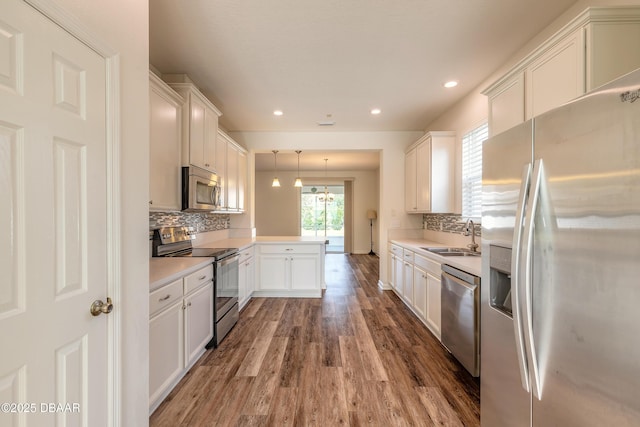 kitchen featuring stainless steel appliances, a peninsula, wood finished floors, a sink, and white cabinets