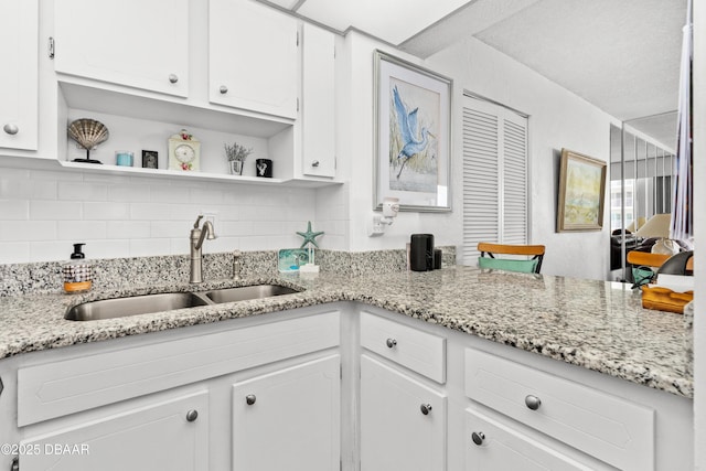 kitchen featuring white cabinetry, light stone counters, sink, and tasteful backsplash