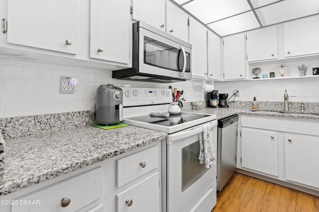 kitchen featuring sink, backsplash, stainless steel appliances, white cabinets, and light wood-type flooring