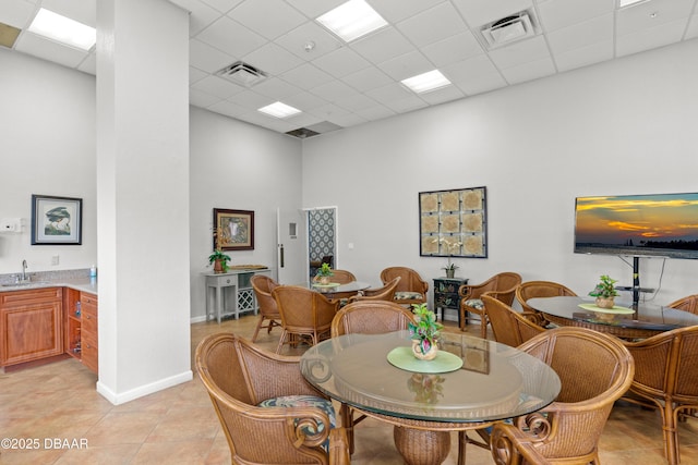 dining space featuring a drop ceiling, sink, light tile patterned floors, and a high ceiling