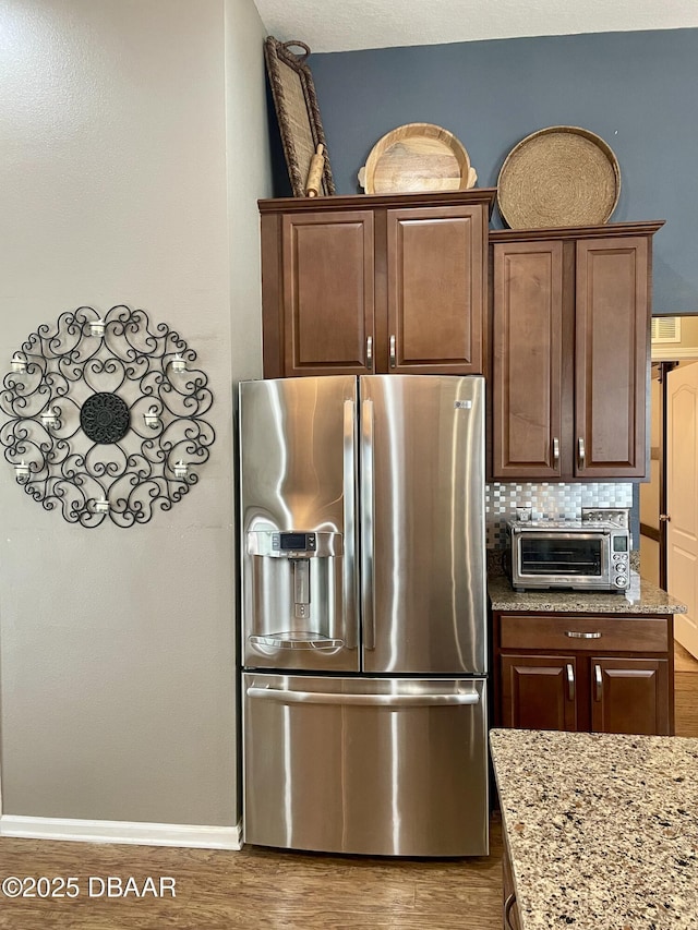 kitchen featuring light stone counters, stainless steel fridge, dark hardwood / wood-style flooring, and decorative backsplash