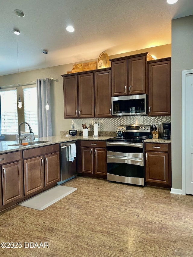 kitchen featuring pendant lighting, sink, backsplash, stainless steel appliances, and light stone counters