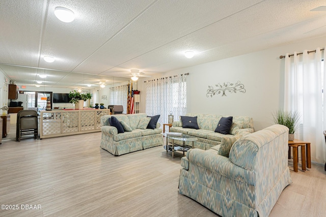 living room featuring light hardwood / wood-style floors, a textured ceiling, ceiling fan, and a healthy amount of sunlight