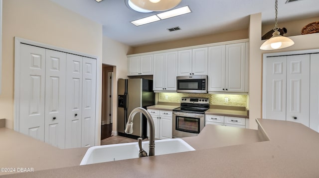 kitchen with stainless steel appliances, decorative backsplash, sink, pendant lighting, and white cabinetry