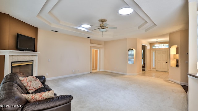 carpeted living room with ceiling fan, a raised ceiling, and a tile fireplace