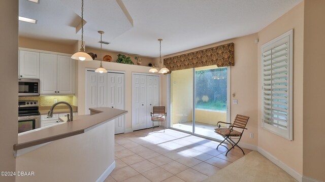 kitchen featuring stainless steel appliances, white cabinets, light tile patterned floors, tasteful backsplash, and decorative light fixtures