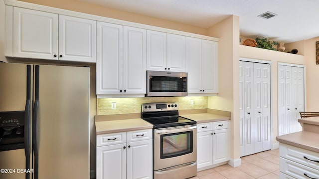 kitchen featuring stainless steel appliances, light tile patterned flooring, white cabinets, and decorative backsplash